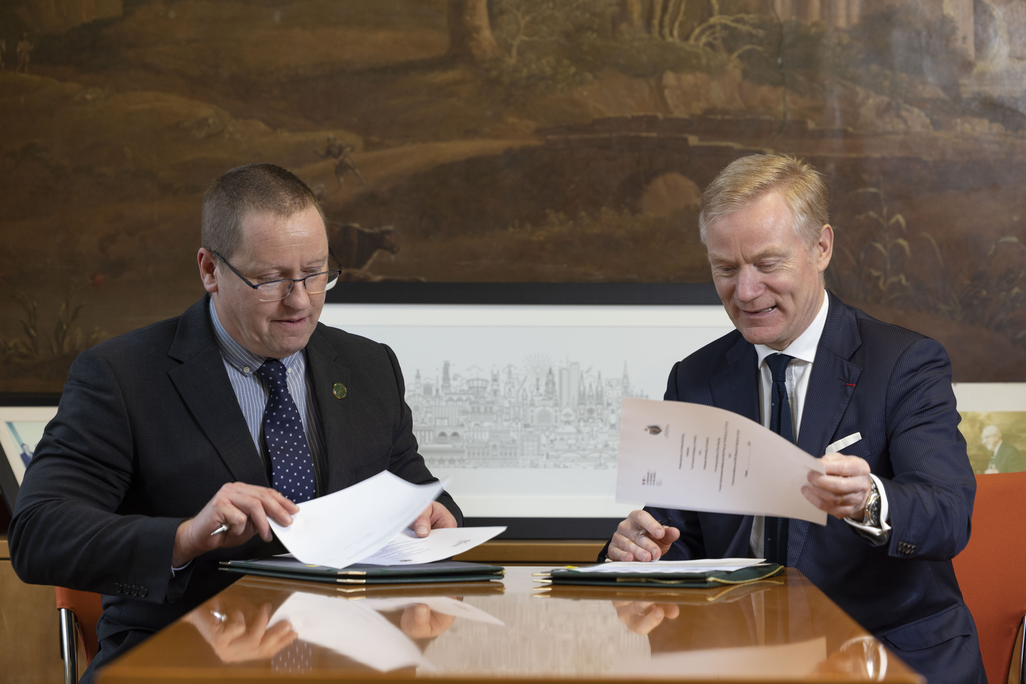 Dr Patrick O'Leary and H.E. Vincent Guérend sitting at a desk in the Registrar's Office of NUI, signing the memorandum of understanding in relation to the NUI - French Embassy collaborative grant.